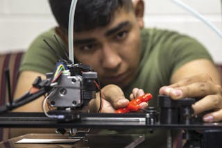 A U.S. Marine makes small adjustments to a 3D printer before loading a design during a class that enables Marines to produce parts quickly with exact specifications and at almost any location.