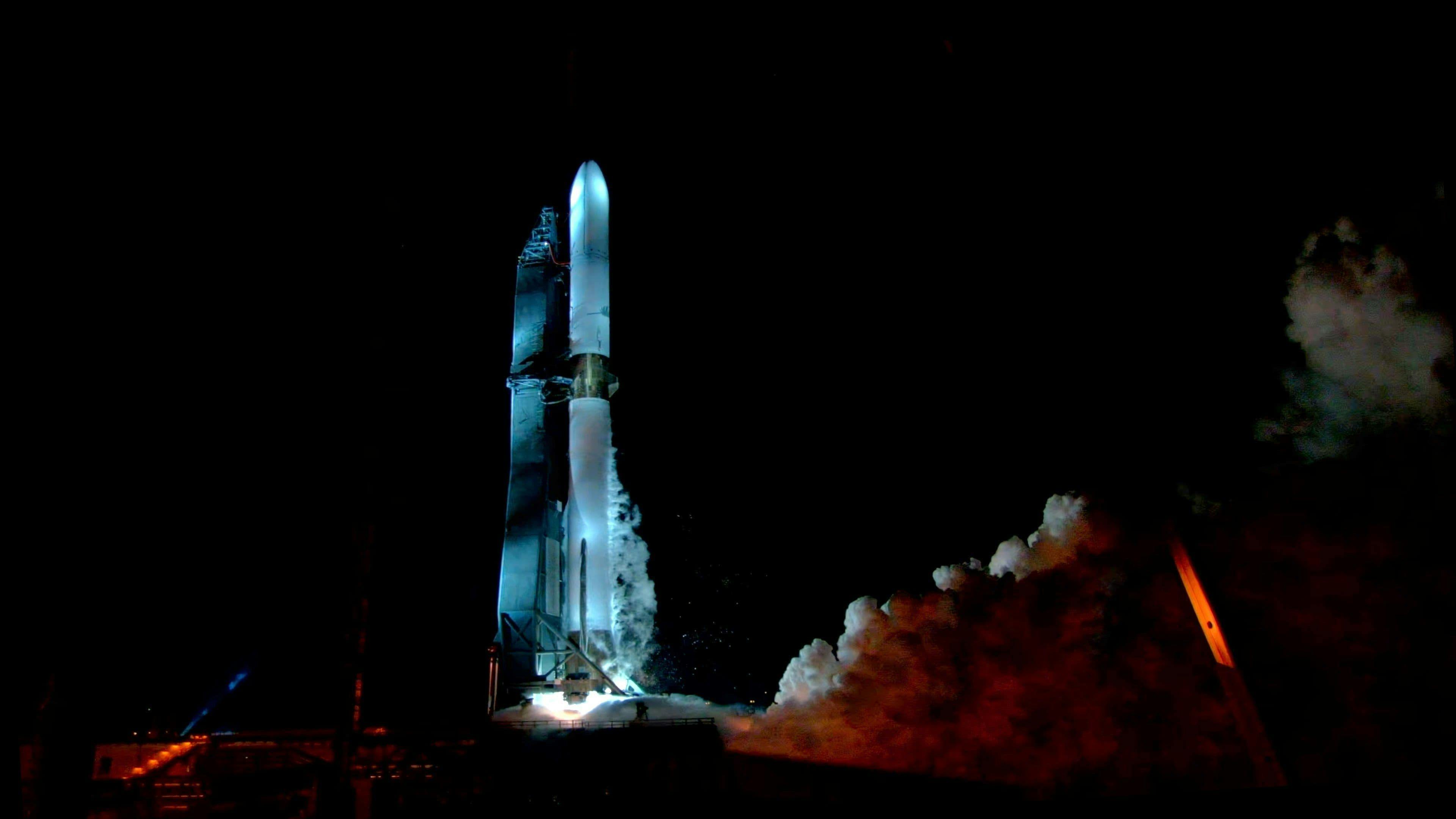 A side profile photo of a Blue Origin rocket firing on the ground at night.
