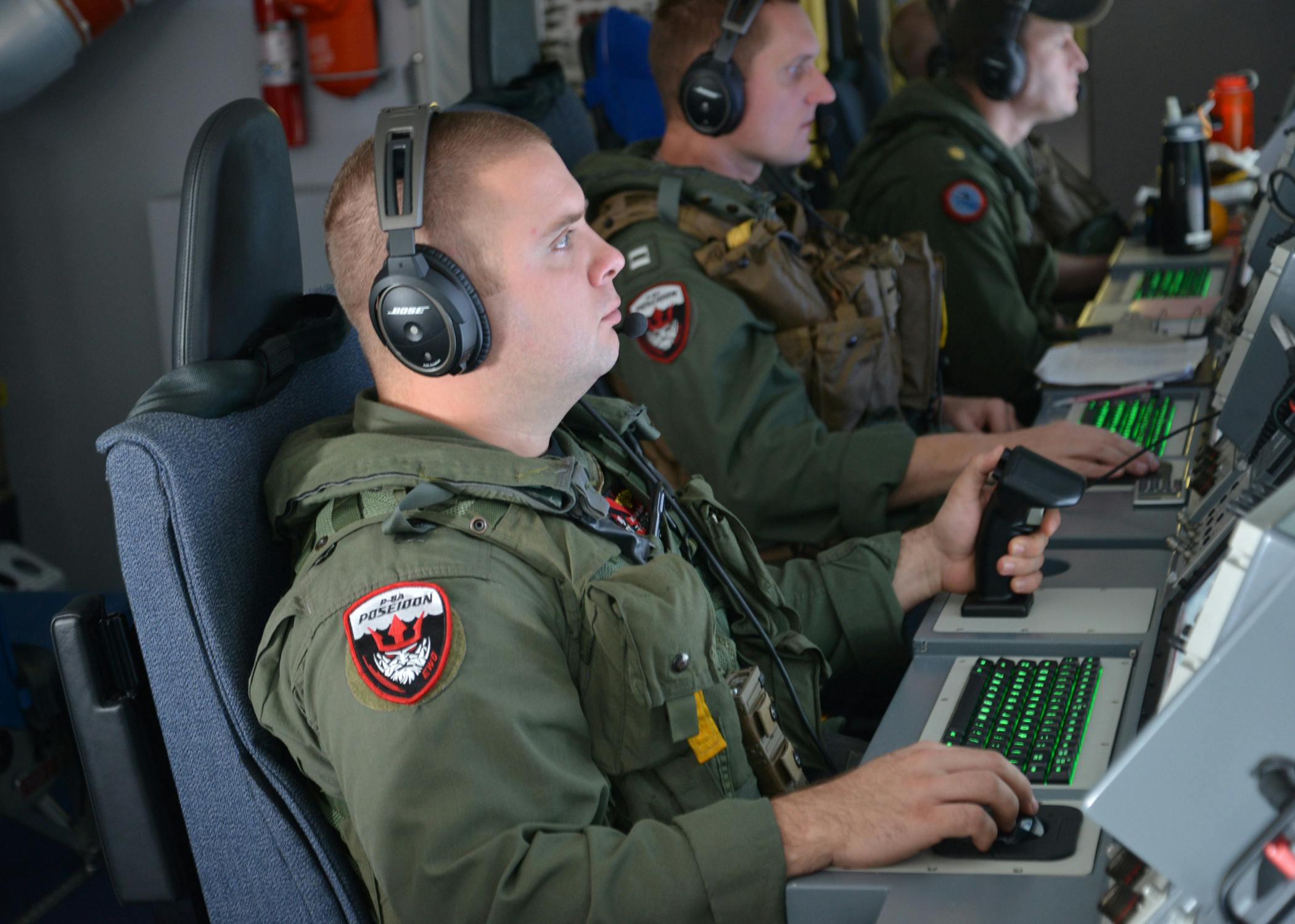 An electronic warfare operator monitors his workstation on a P-8A Poseidon maritime surveillance jet during a mission to assist in search and rescue efforts.