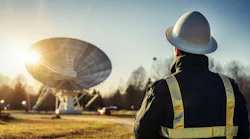 A man in a hard hat looks at a terrestrial satellite dish from the distance