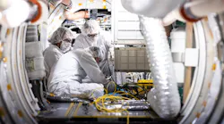 A trio of people in cleanroom suits work with electronics.