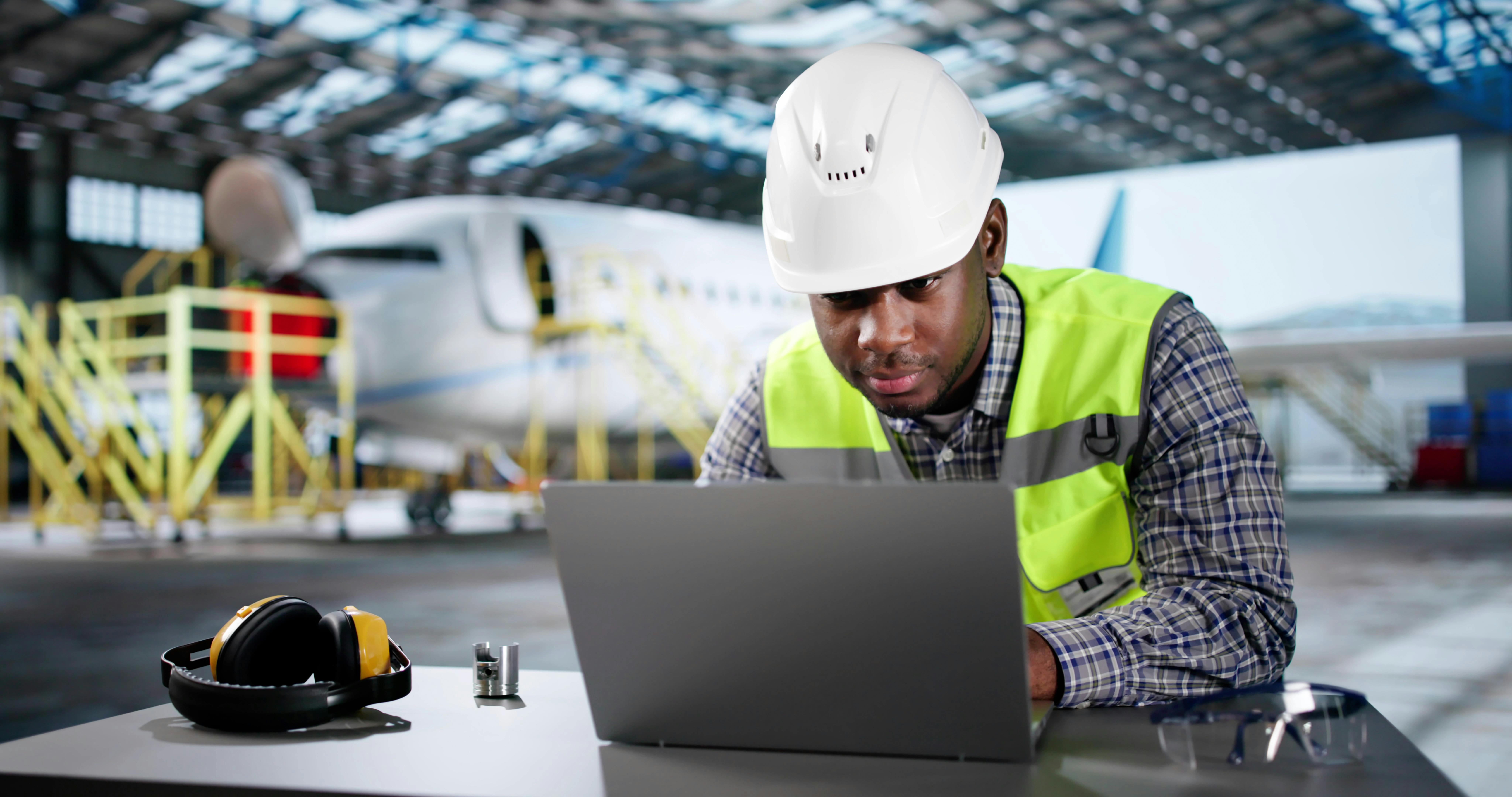 A technician works on a laptop in an airplane hanger