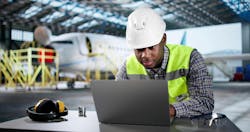 A technician works on a laptop in an airplane hanger A technician works on a laptop in an airplane hanger
