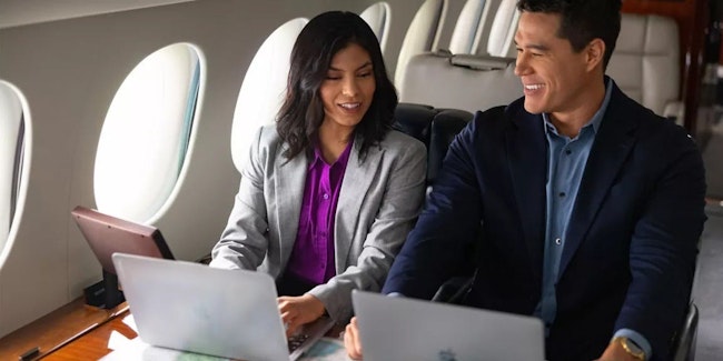 A man and a woman work on laptops side-by-side on a business jet.