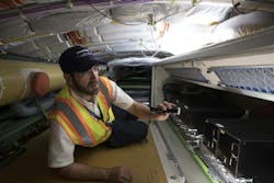 A tech service worker uses a flashlight to inspect equipment in an airplane. A tech service worker uses a flashlight to inspect equipment in an airplane.