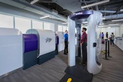 A man walks through a CT scanner at an airport. A large piece of equipment is next to it. A man walks through a CT scanner at an airport. A large piece of equipment is next to it.