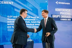Representatives of Embraer and Lukasiewicz shake hands on a stage Representatives of Embraer and Lukasiewicz shake hands on a stage