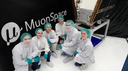 A group of people in cleanroom clothing pose in front of a satellite