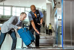 A JetBlue employee directs a passenger to place their bag on a stand. A JetBlue employee directs a passenger to place their bag on a stand.