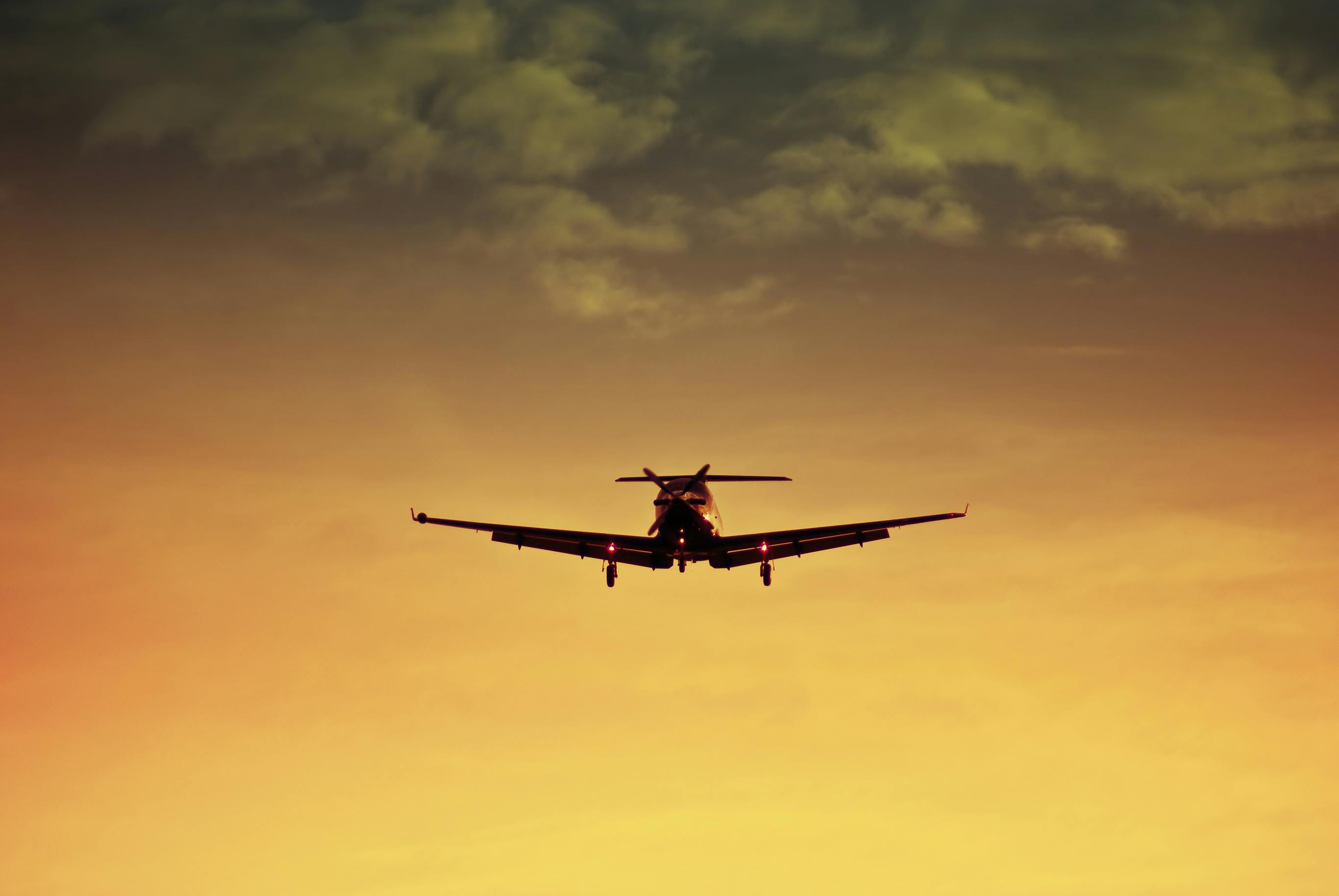 A prop plane landing as the sun sets behind it