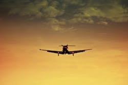 A prop plane landing as the sun sets behind it A prop plane landing as the sun sets behind it