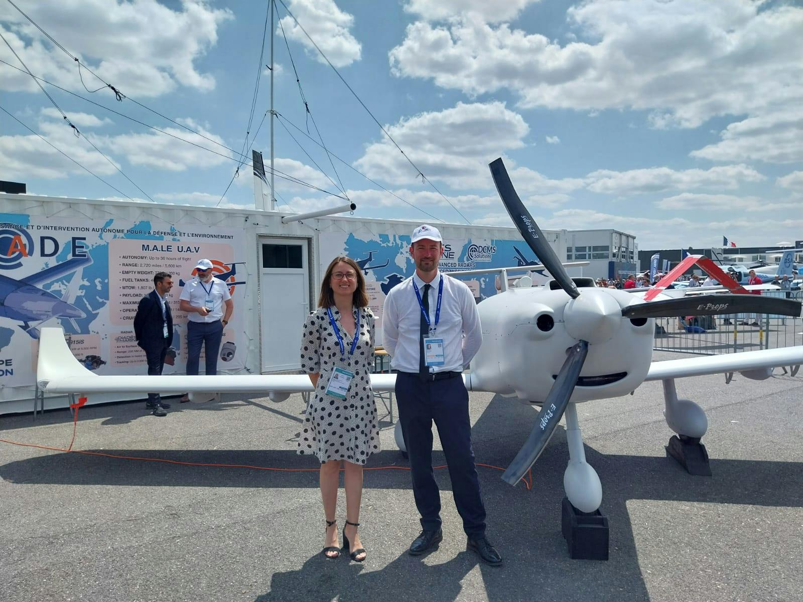 A photo of a man and a woman standing next to an uncrewed aircraft on the tarmac.