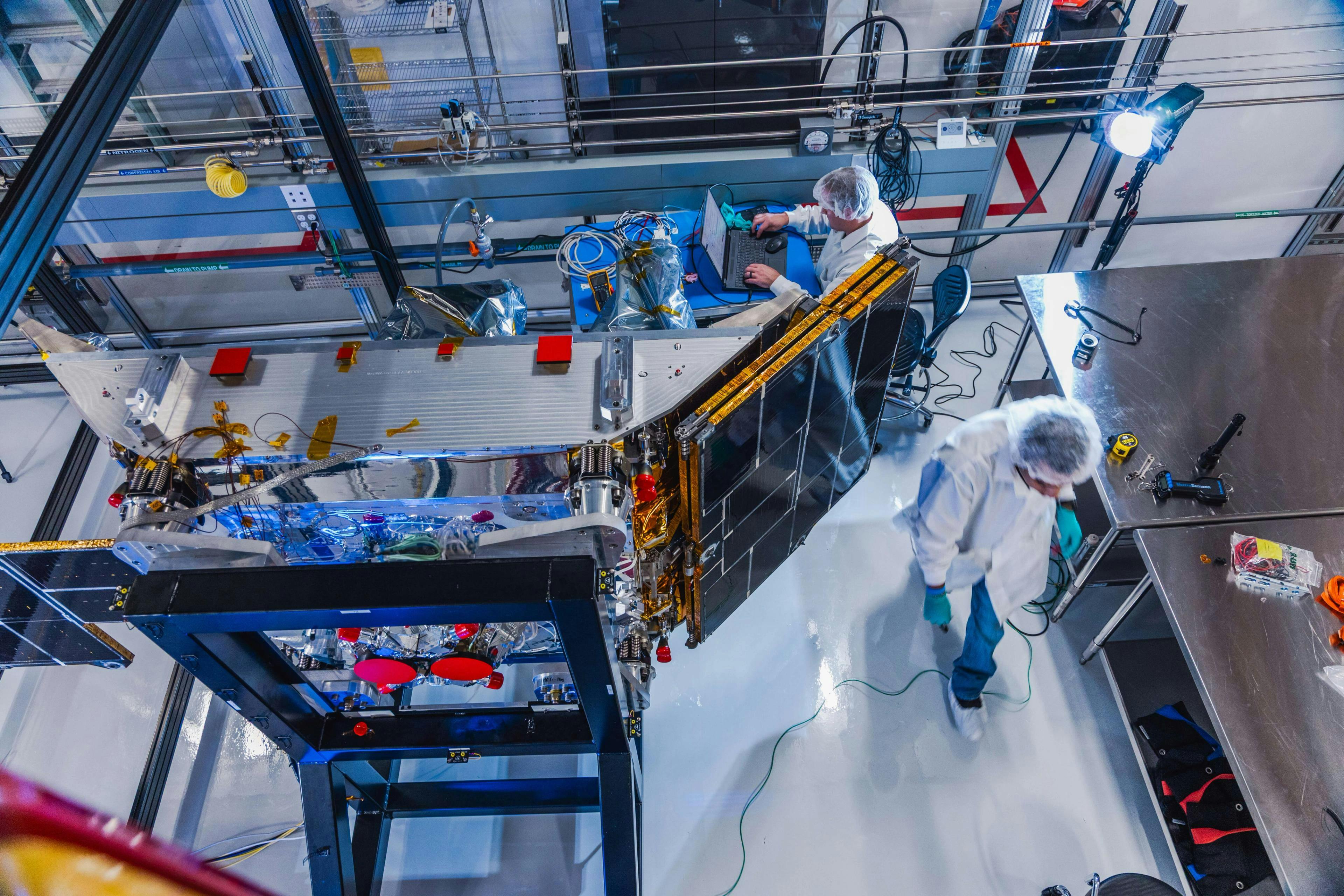 Two workers in a cleanroom facility along with Impulse Space's technology