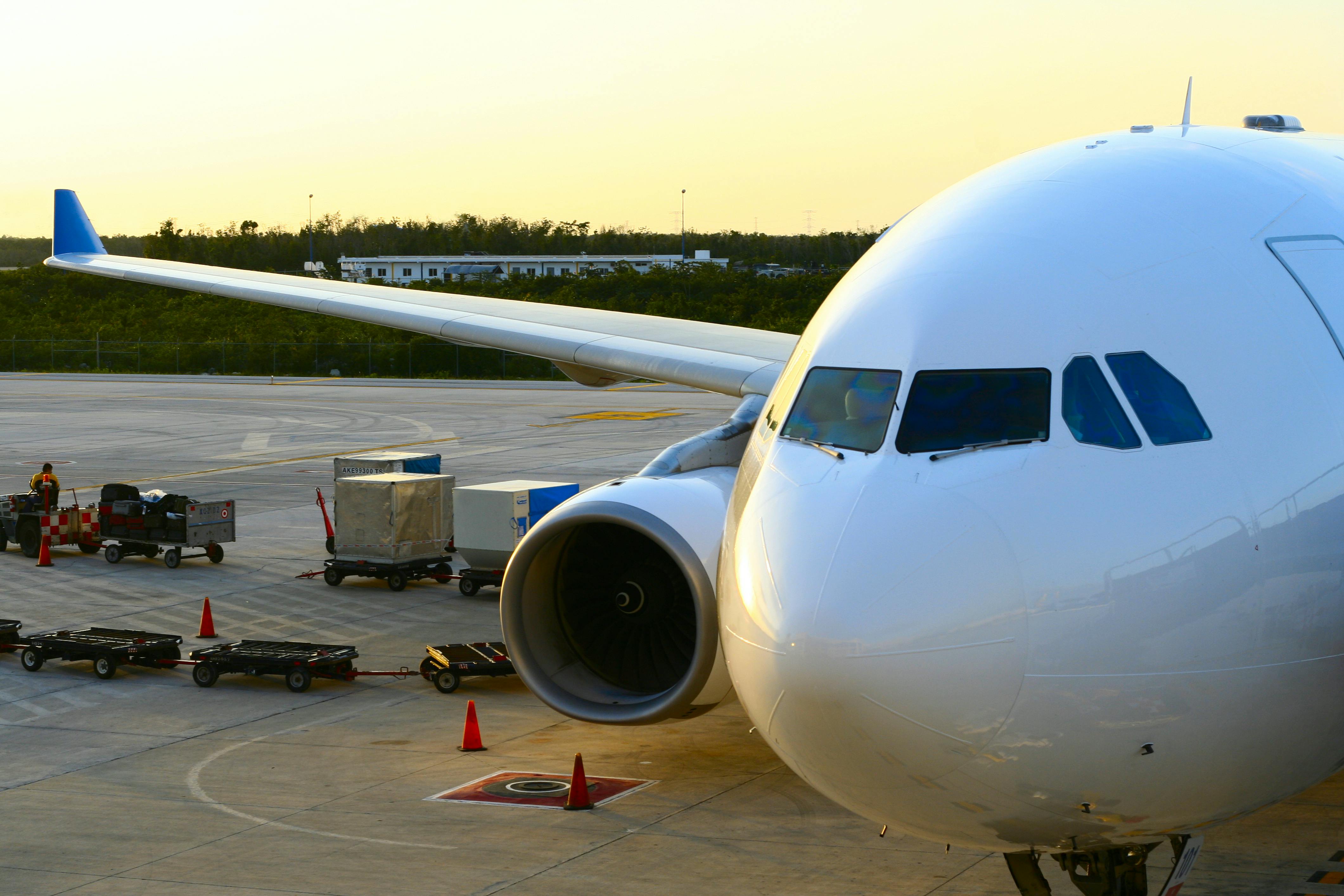 An aircraft on the tarmac as workers load or unload baggage.