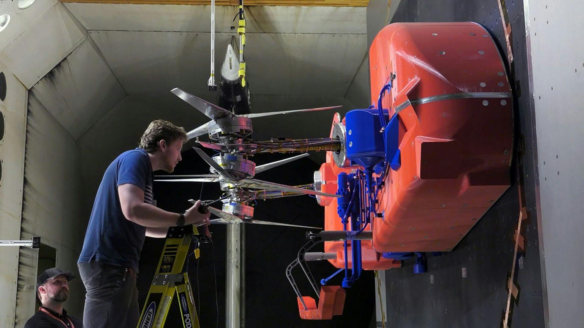 Technicians install and adjust the rotors on the full-scale test model representing half of the Dragonfly lander in the Transonic Dynamics Tunnel facility at NASA&rsquo;s Langley Research Center. During a month-long testing campaign, the team was able to evaluate rotor system performance in Titan-like conditions. NASA photo.