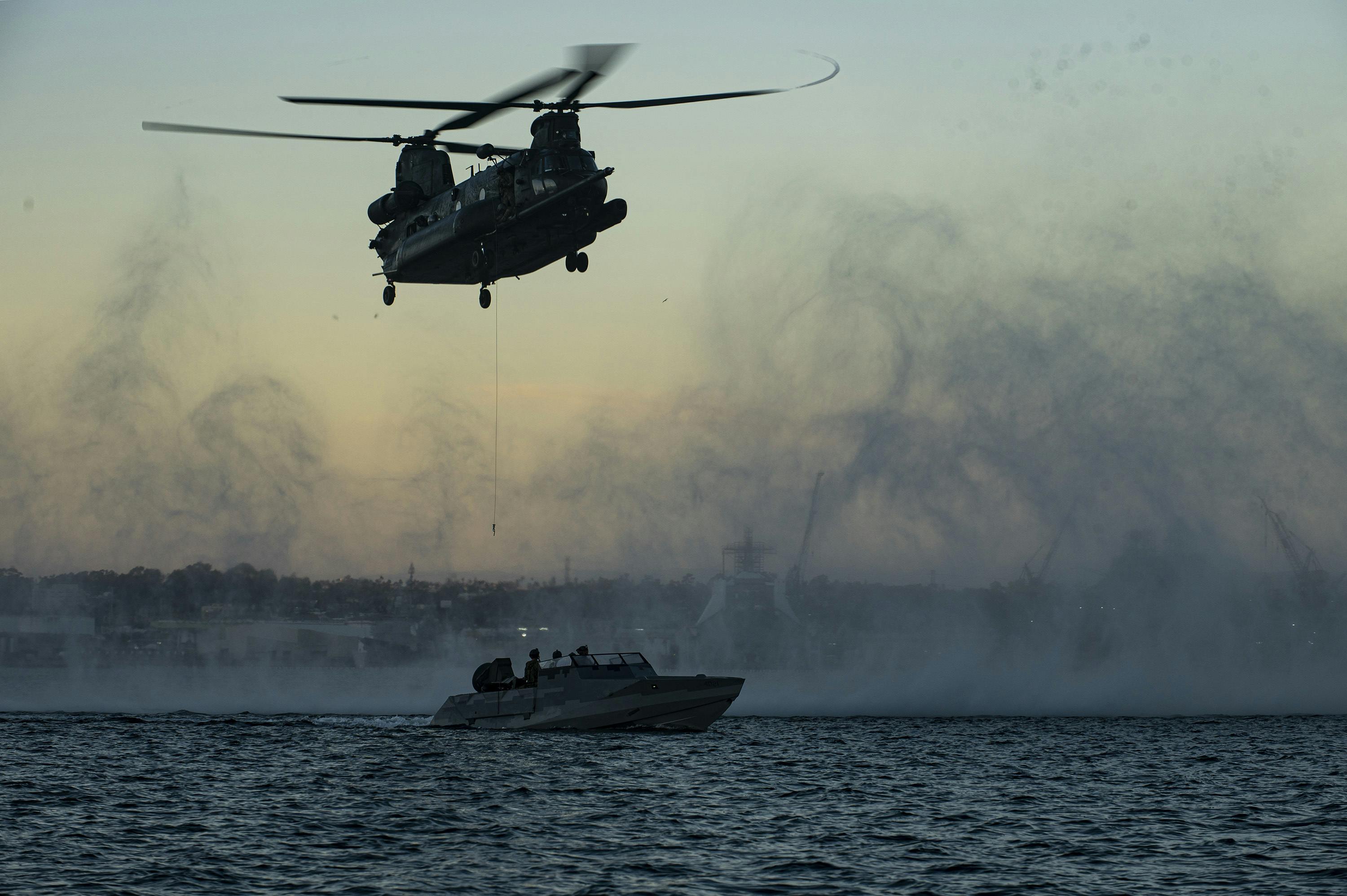 A U.S. MH-47 Chinook heavy assault helicopter lowers a hoist cable to a combatant craft during a maritime training evolution.