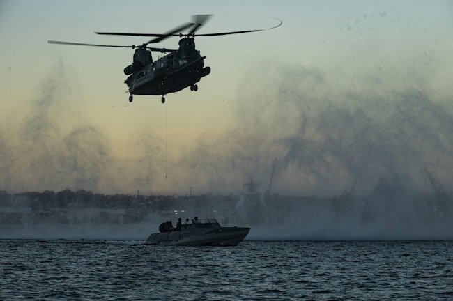 A U.S. MH-47 Chinook heavy assault helicopter lowers a hoist cable to a combatant craft during a maritime training evolution.