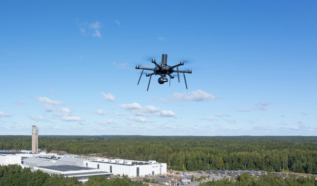 A small electric UAV flies at an industrial site.