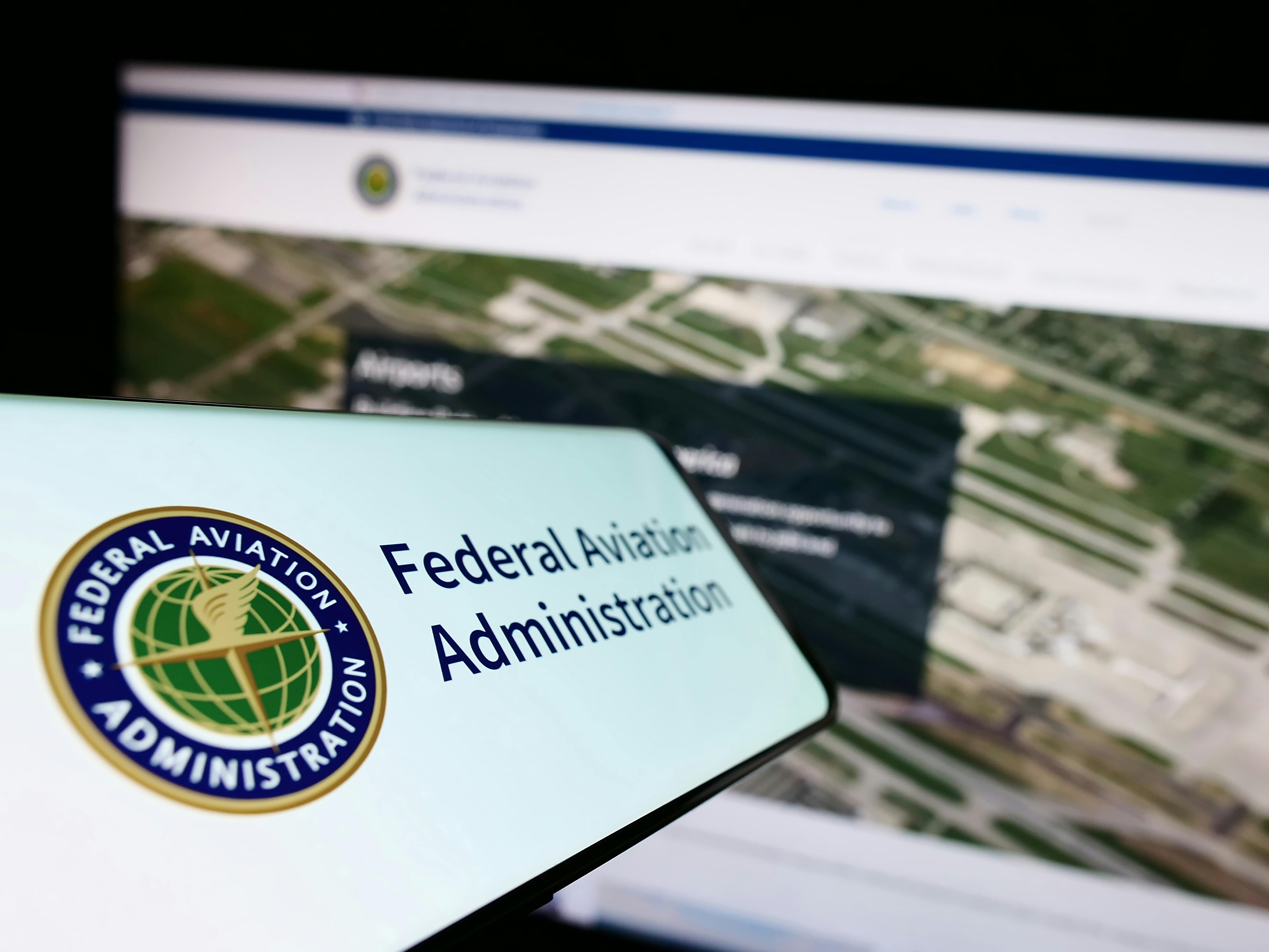 Cellphone with seal of US Federal Aviation Administration (FAA) on screen in front of website. Focus on center-left of phone display