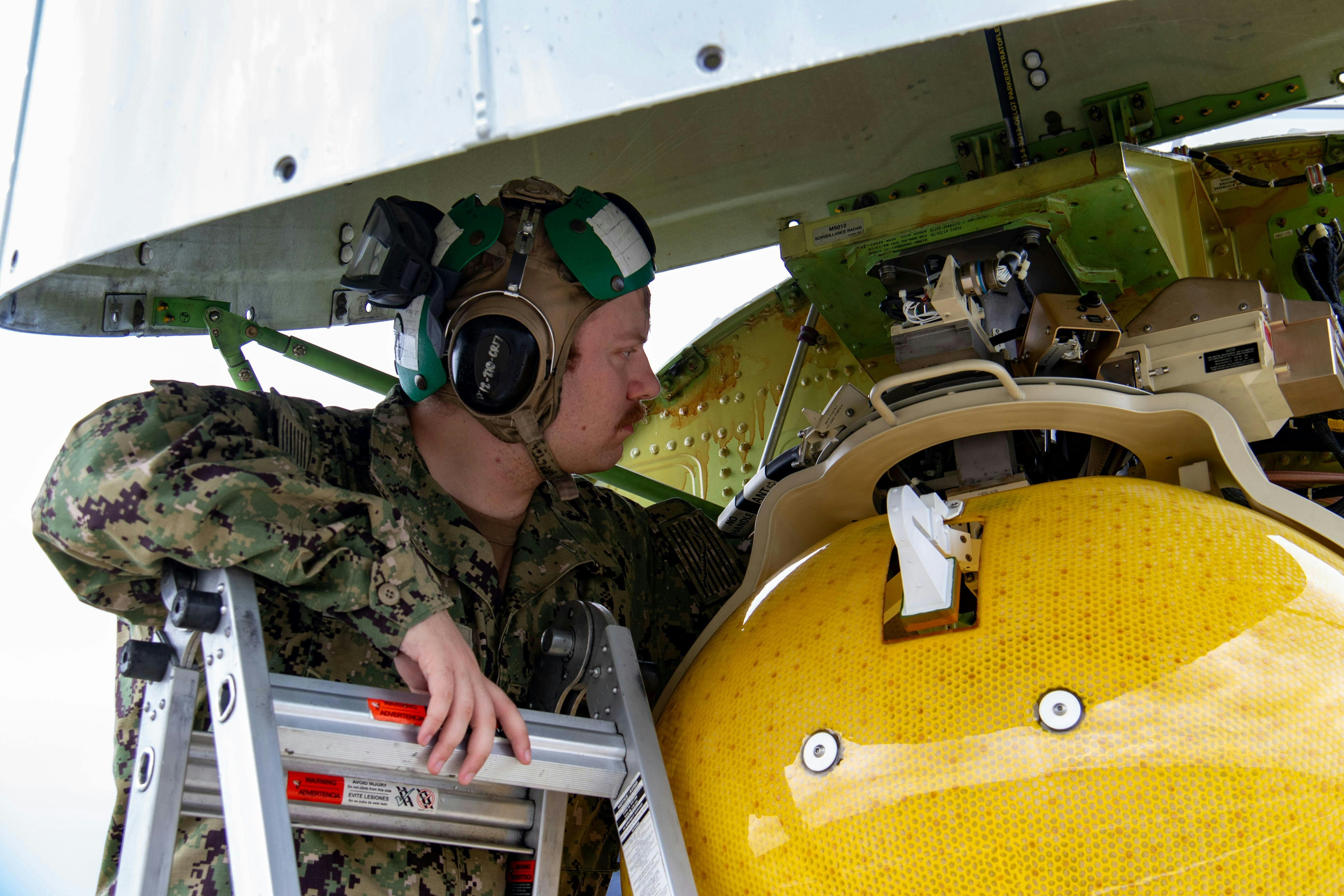 A U.S. Navy aviation electronics technician performs maintenance on the AN/APY-10 radar of a P-8A Poseidon at Royal Air Force Base Lossiemouth, Scotland, in 2023.