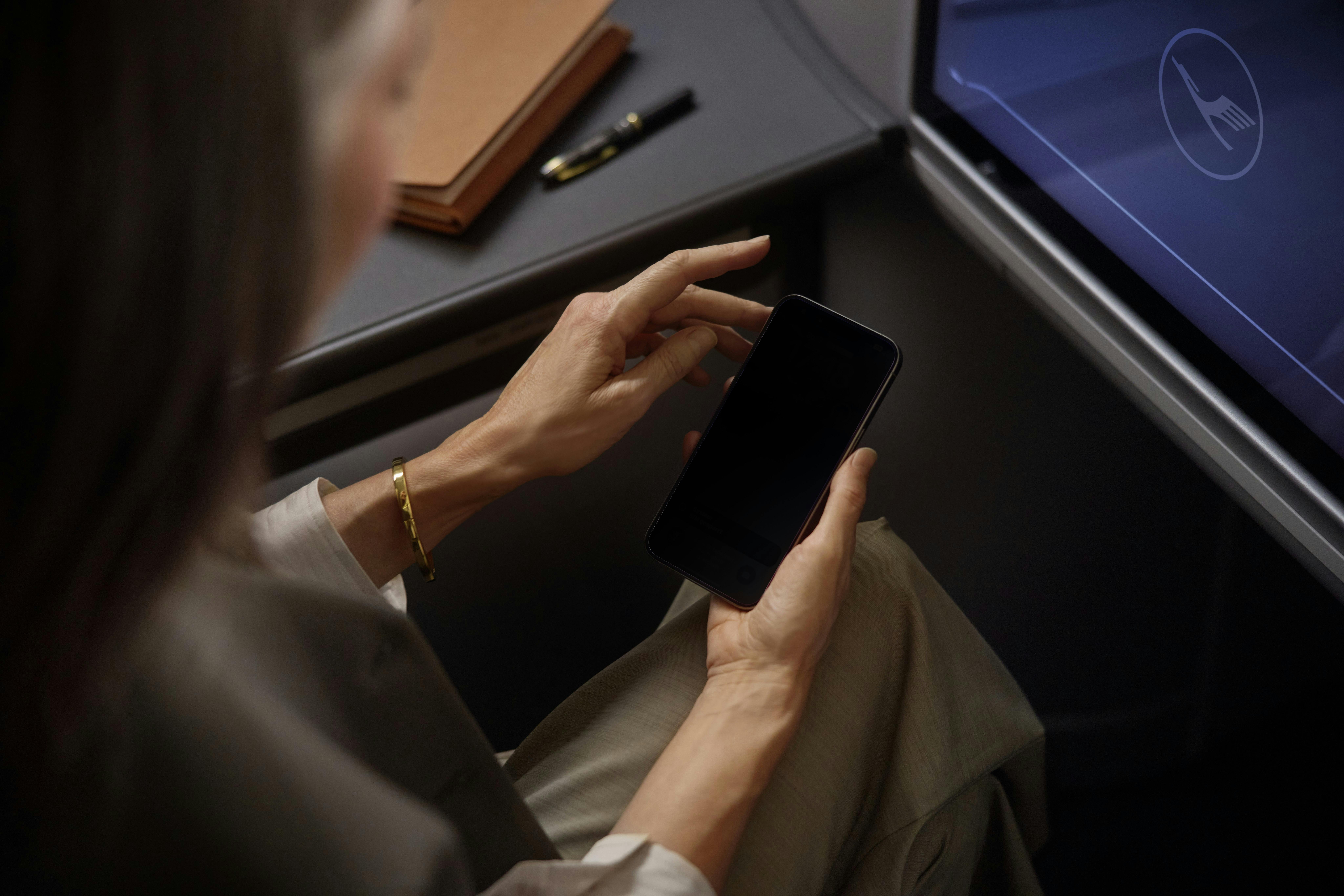 A passenger looks at an electronic device while seated in a Lufthansa seat.