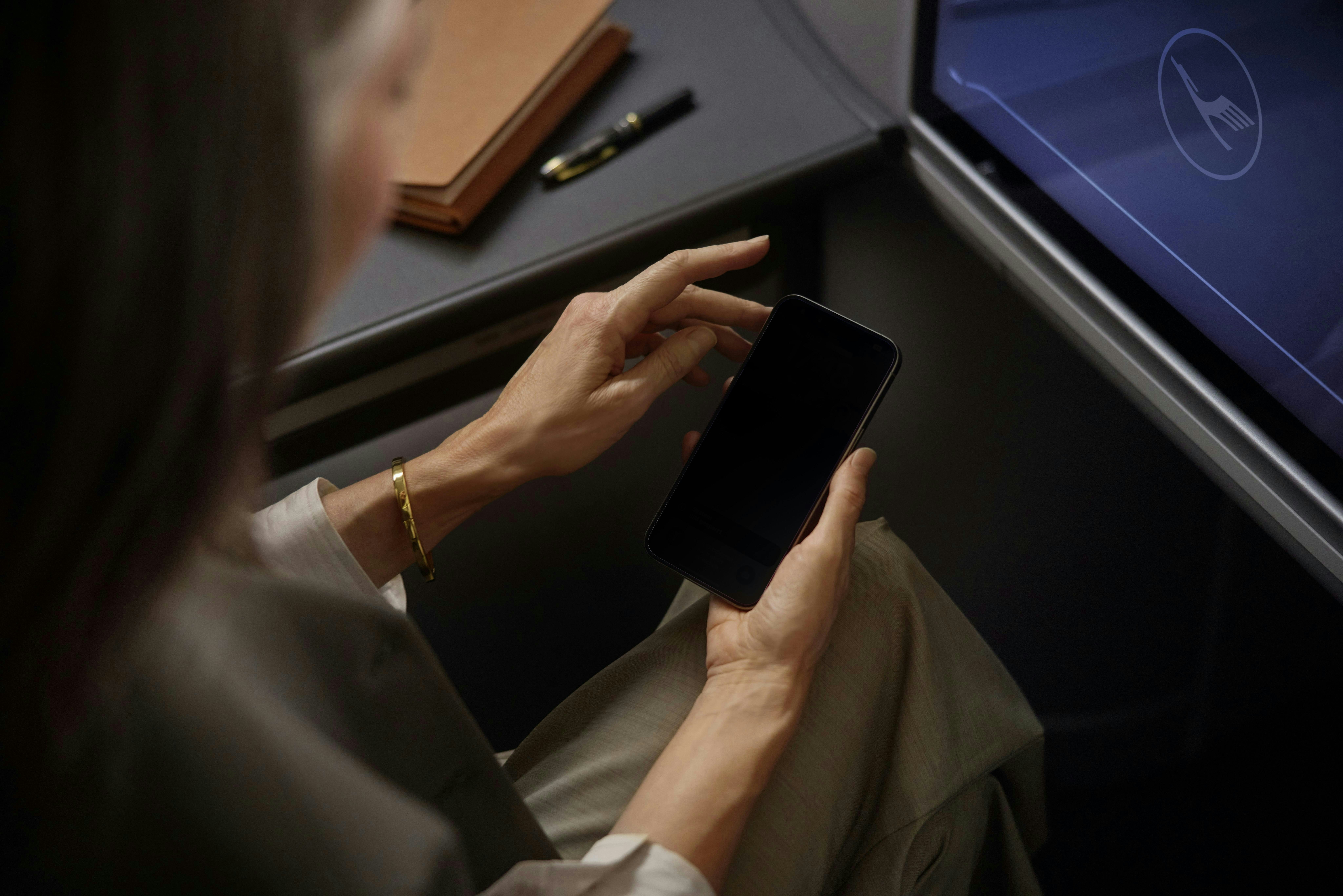 A passenger looks at an electronic device while seated in a Lufthansa seat.