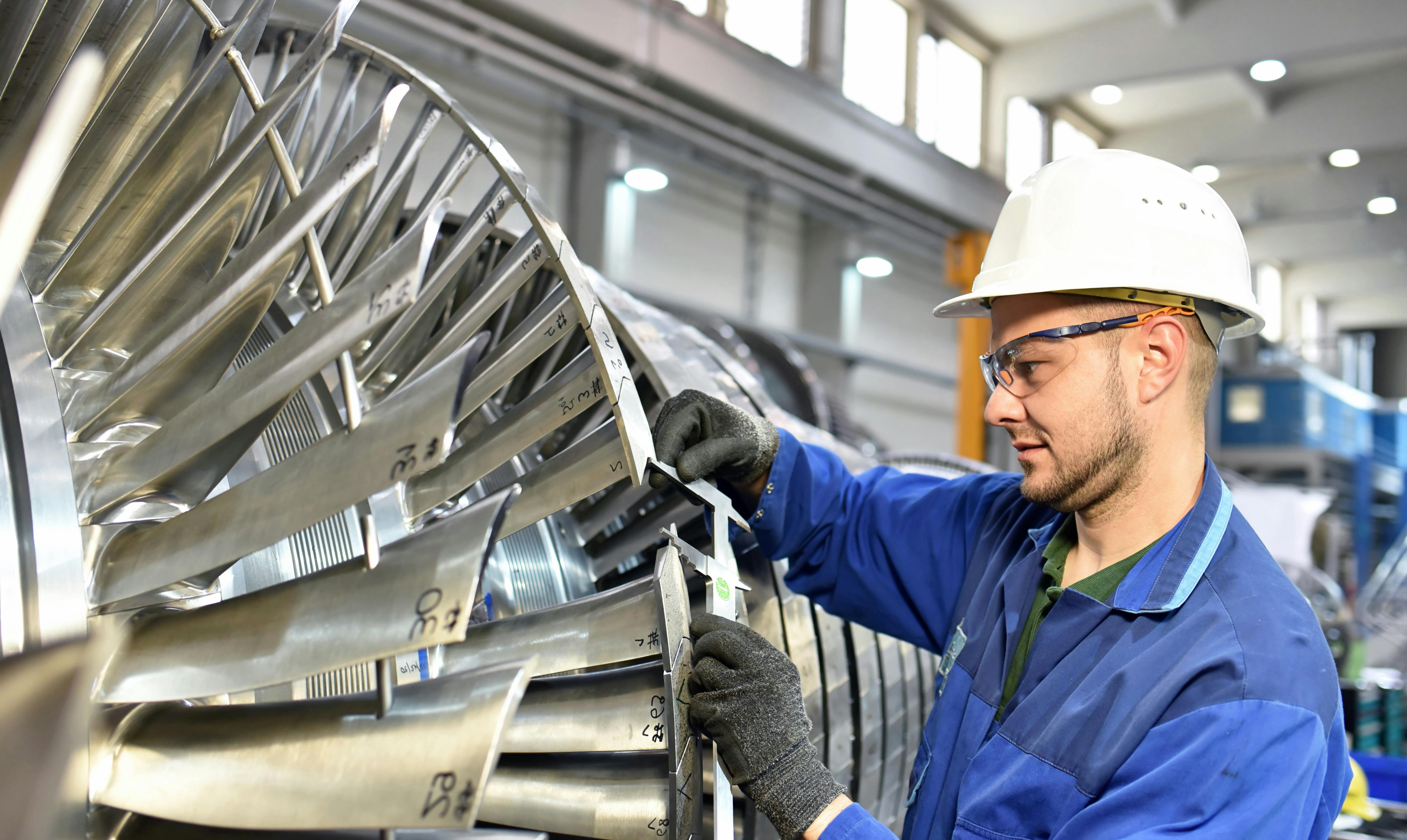 A factory worker performs a task on a turbine.
