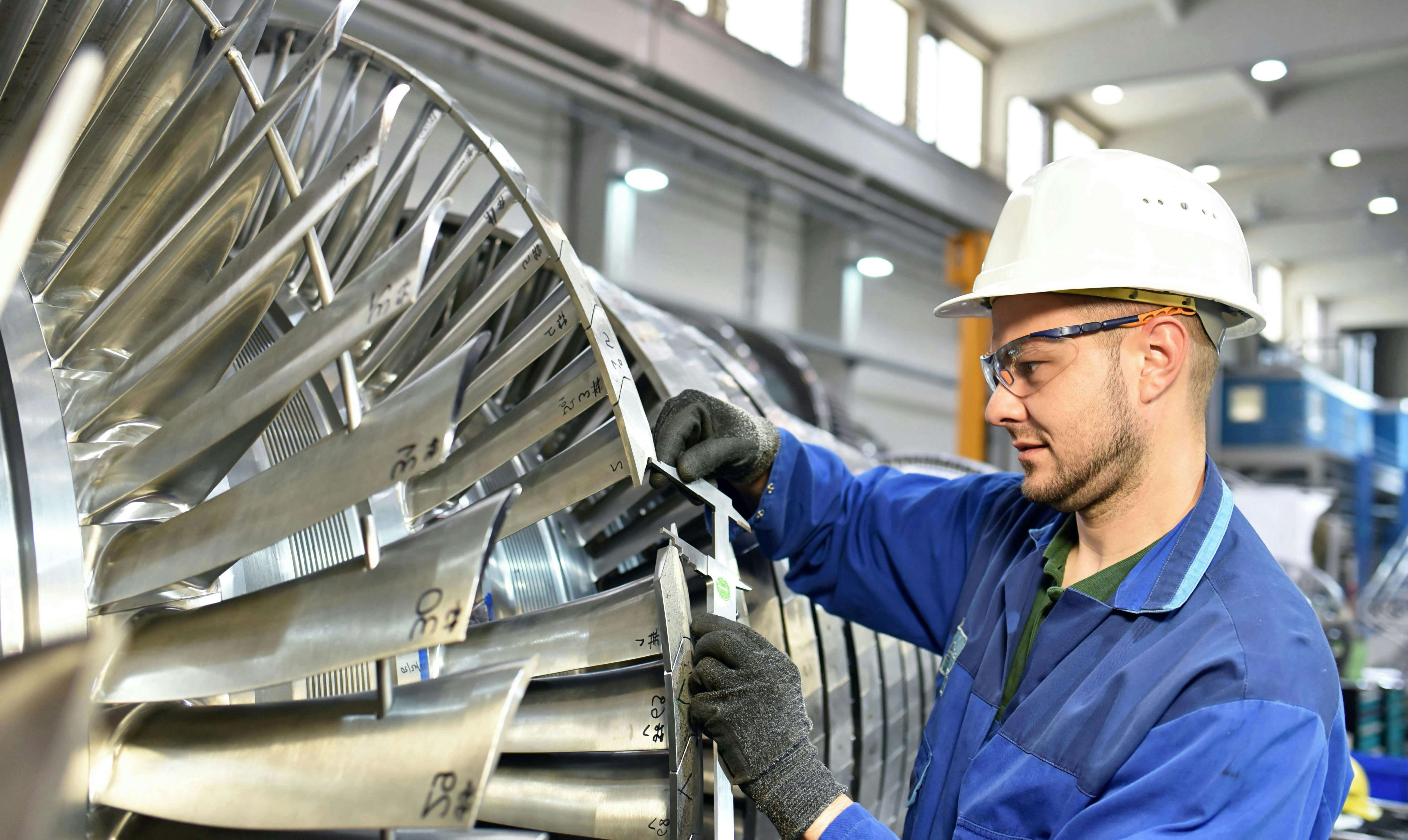 A factory worker performs a task on a turbine.