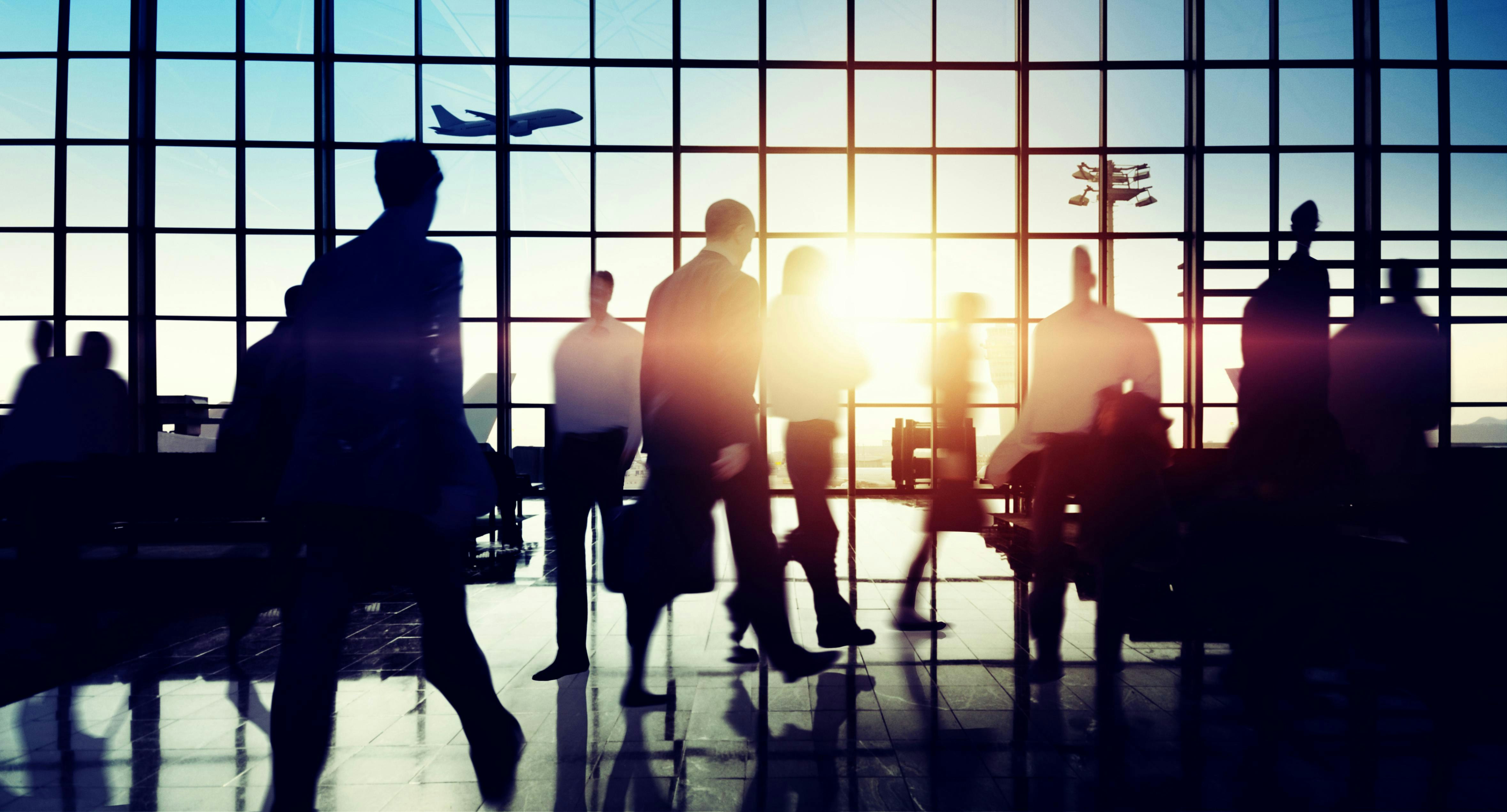 People in an airport terminal shown mostly in shadow.