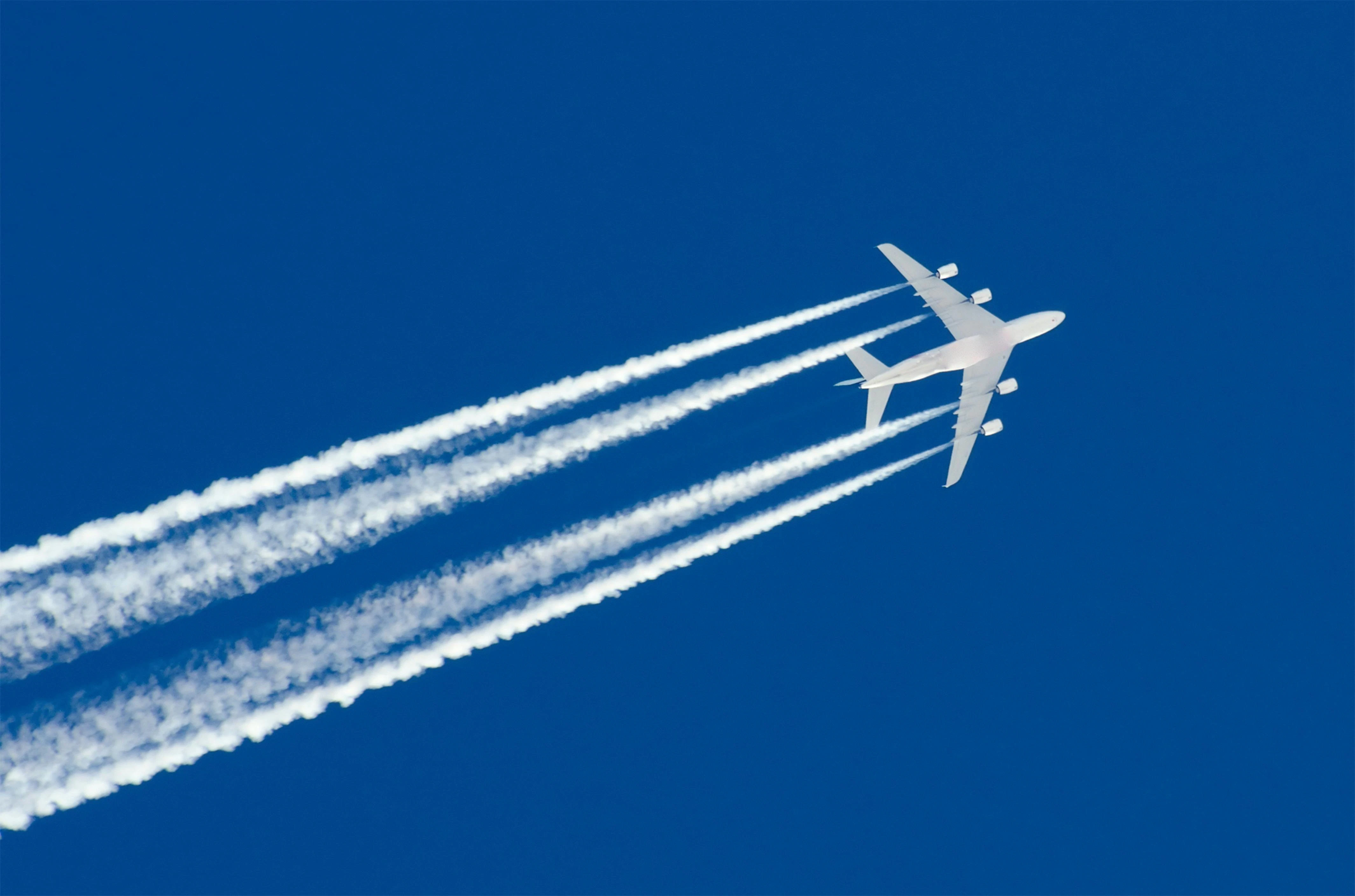 An aircraft and its contrails seen flying above in a blue sky