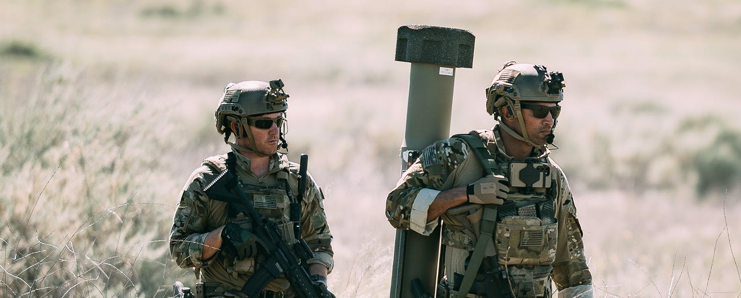 Two soldiers in field BDUs walk. One carries a rifle, the other, the Switchblade 400.