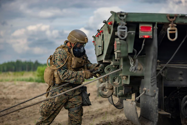 U.S. Marine Corps Lance Cpl. Logan Webster, a motor vehicle operator with Combat Logistics Battalion 24, Combat Logistics Regiment 27, 2nd Marine Logistics Group, attaches a winch to a medium tactical vehicle replacement during exercise Baltic Operations 26 in Skrunda, Latvia. The Department of Defense is asking industry for information as it looks to automate the labor-intensive and dangerous work of recovering vehicles from the field. U.S. Marine Corps photo by Lance Cpl. Brady Hathaway.
