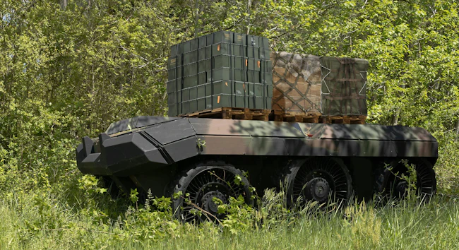 A six-wheeled, flat-topped uncrewed vehicle carries ammo containers and other materiel in a grassy field
