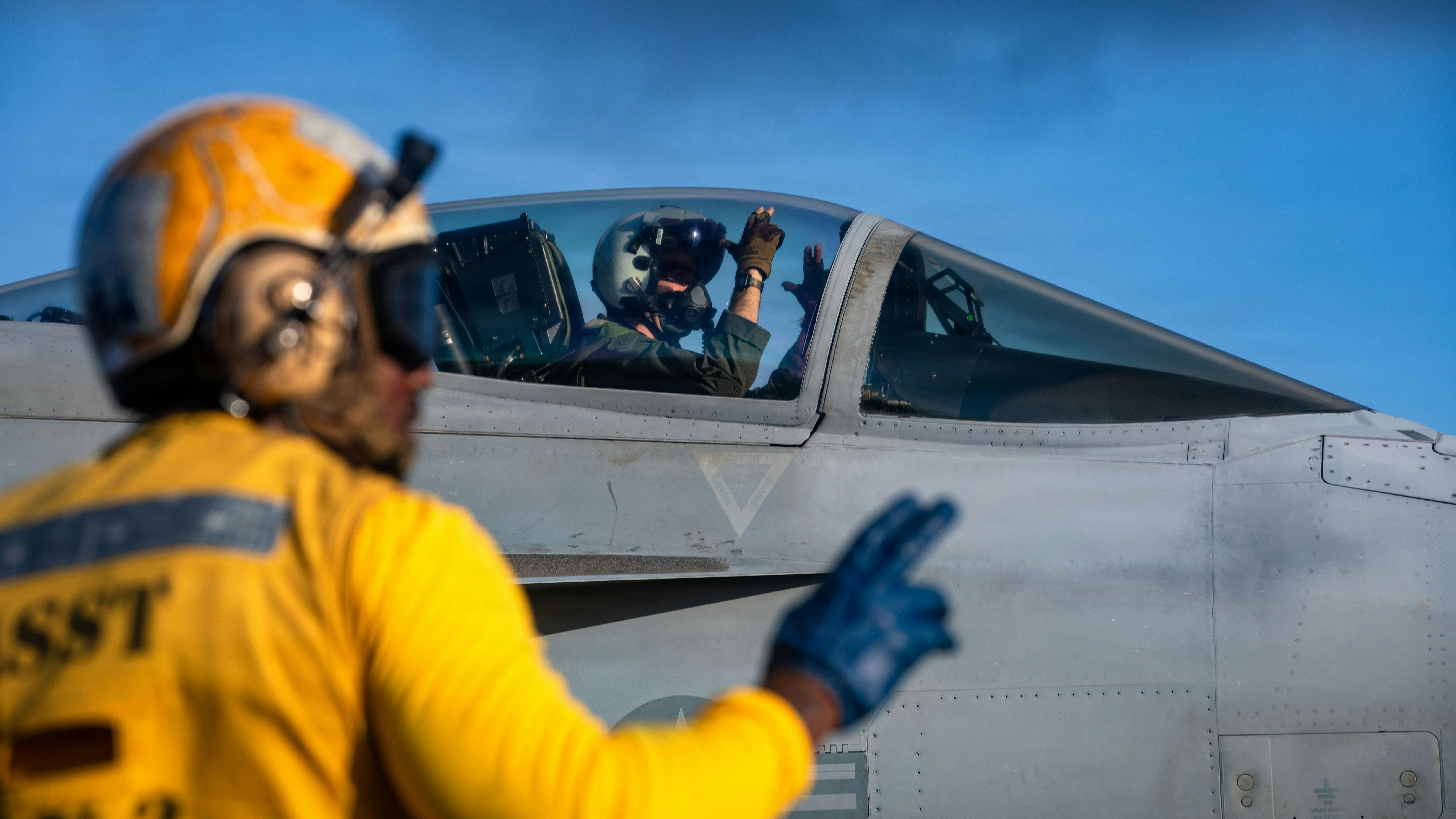 A U.S. Sailor communicates with flight deck personnel via hand signals before takeoff in an F/A-18E Super Hornet aircraft, attached to Strike Fighter Squadron 87, on the flight deck of the aircraft carrier USS Gerald R. Ford (CVN 78). U.S. Navy photo.