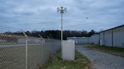 A site perimeter: a fence line, a slim mast carrying two panel antennas and a dome, an equipment cabinet, and a small quadcopter in the distance. No real site is depicted.